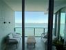 Covered balcony featuring large-format stone-finish floor tiles, wall-mounted exterior lighting, and a glass-paneled railing overlooking the water