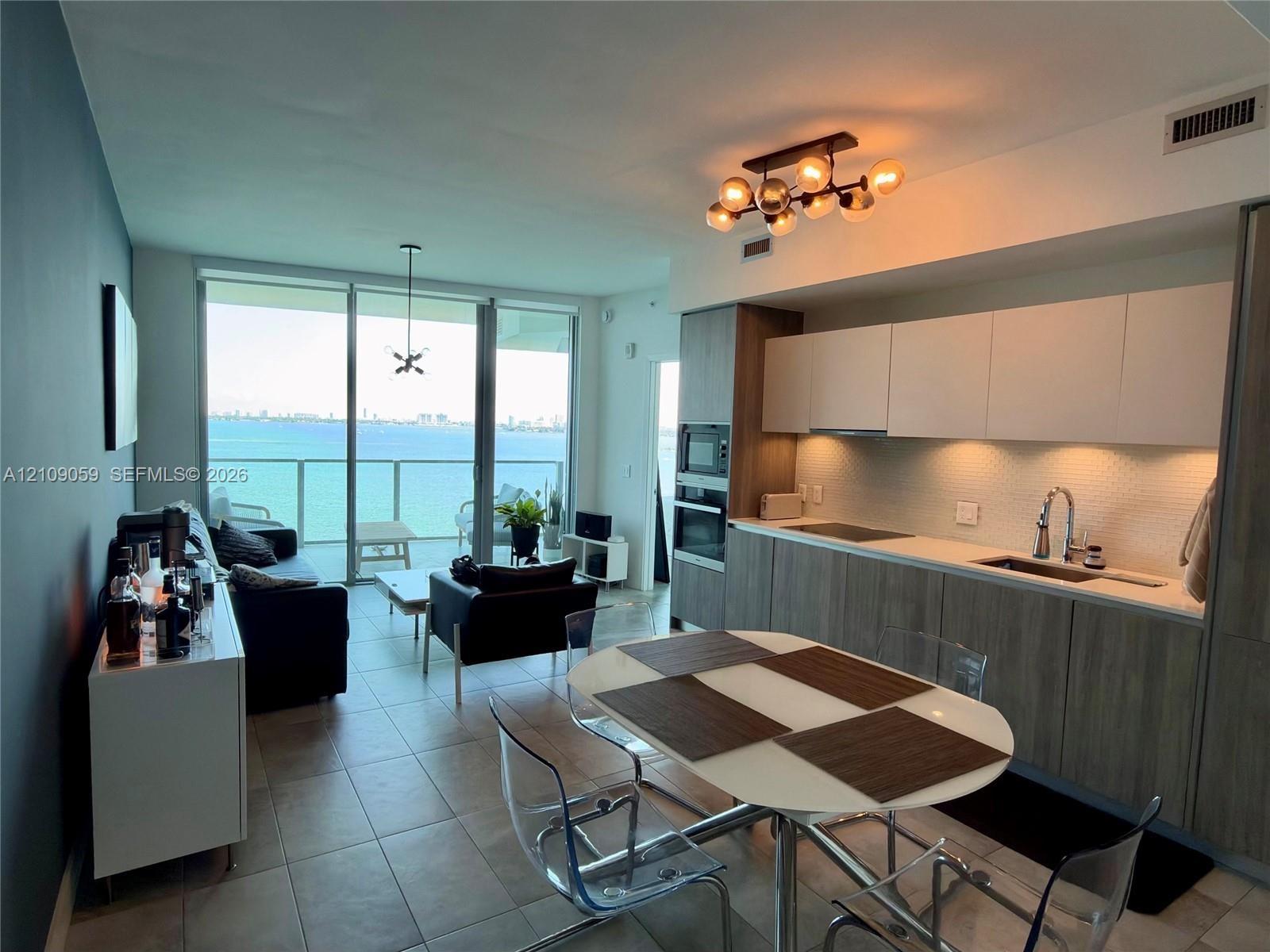 Open-concept interior featuring floor-to-ceiling glass doors, built-in cabinetry with matte finish, tile flooring, integrated kitchen appliances, and 