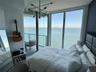 Floor-to-ceiling windows, private balcony with glass railing, contemporary sputnik-style chandelier, and water backdrop