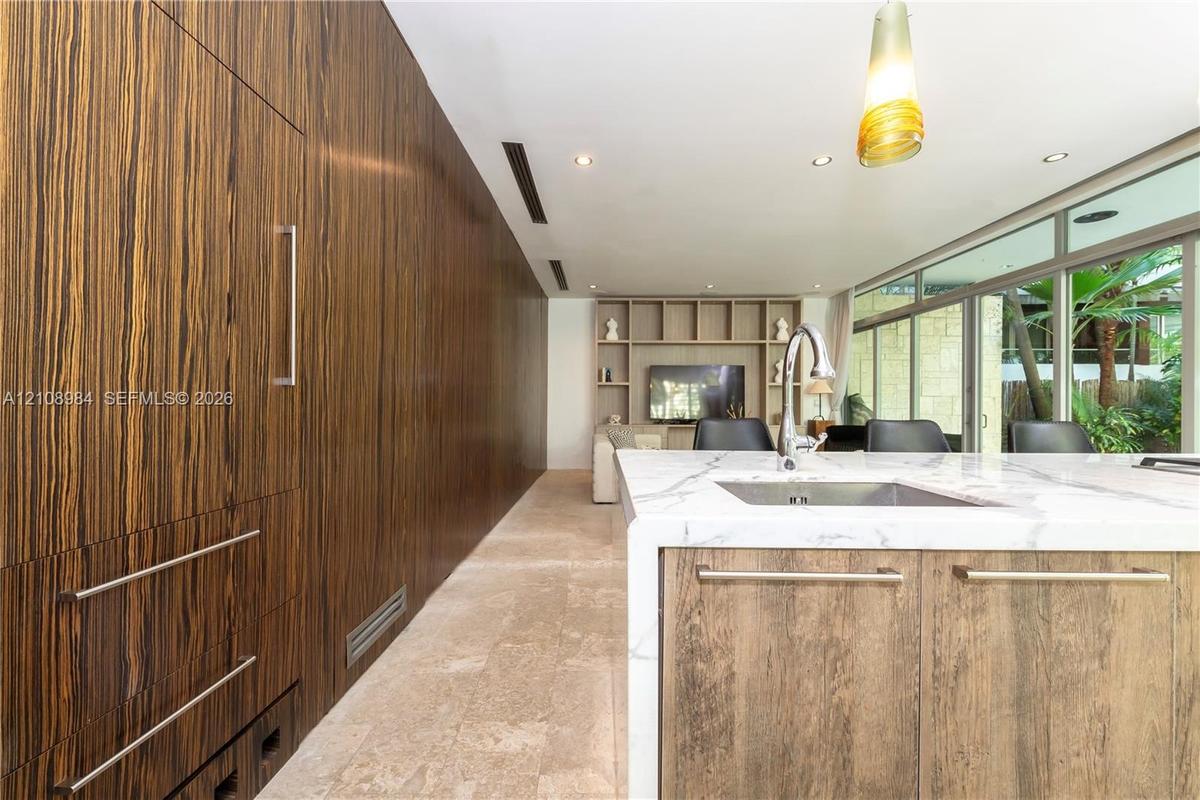 Floor-to-ceiling wood-veneer cabinetry, stone-surfaced kitchen island with a waterfall edge, stone flooring, floor-to-ceiling glass wall, and custom b