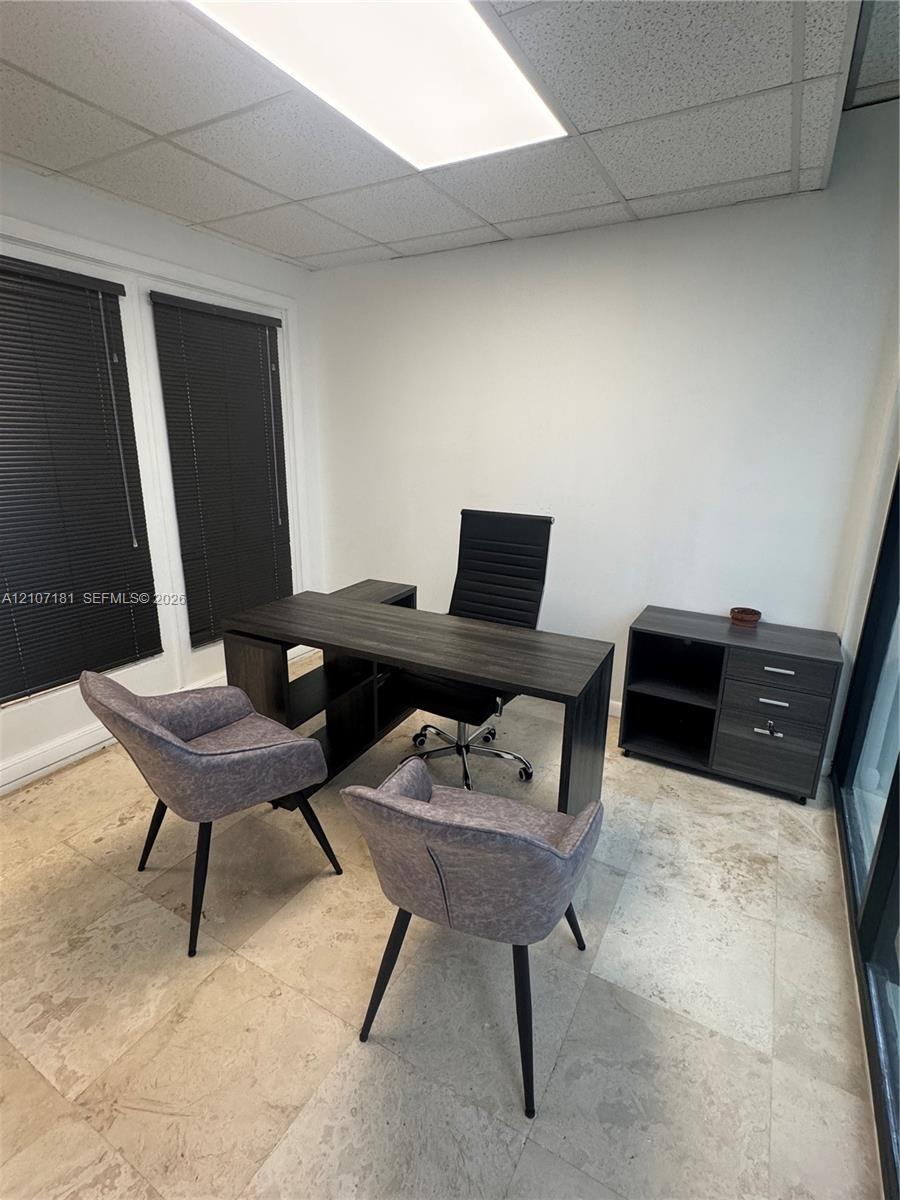 Office featuring stone tile flooring, dual windows with fitted blinds, and a recessed ceiling panel