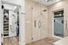 Walk-in shower featuring floor-to-ceiling stone tile, a glass enclosure, a rainfall showerhead, and a wall-mounted hand shower, paired with a built-in