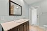 Vanity featuring a stone-surface countertop, rectangular vessel sink, wall-mounted faucet, framed wall mirror, and dark-finish cabinetry with metallic