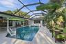 Screen-enclosed swimming pool featuring a Baja shelf, natural stone patio, and covered patio area