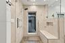 Walk-in shower featuring large-format neutral stone wall tile, multi-head shower system with a rain shower head, built-in stone bench with integrated 