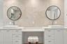 Dual white cabinetry with white stone countertops, integrated center vanity station, dual vessel sinks, wall-mounted round mirrors with matte black fr