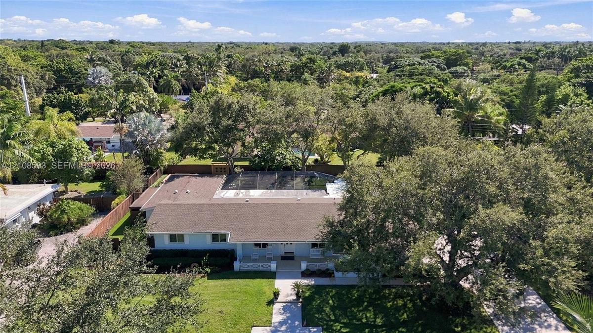 Aerial perspective featuring a single-story residence with a multi-hipped roof, a screened-in rear enclosure, a paved driveway, and mature landscaping