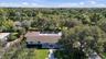 Aerial perspective featuring a single-story residence with a multi-hipped roof, a screened-in rear enclosure, a paved driveway, and mature landscaping