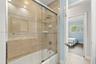 Bathtub and shower combination with floor-to-ceiling neutral tone tile surround, sliding glass enclosure, integrated corner shelving, and chrome fauce