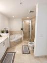 Bathroom featuring a jetted corner soaking tub, a tiled walk-in shower with a glass enclosure, stone-surround finishes, a white vanity with hardware, 