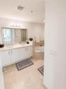 Double vanity with integrated sinks, neutral solid-surface countertop, full-width mirror, and tile flooring with a separate soaking tub featuring ston