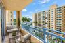 Covered balcony with a protective blue railing, stone-finish flooring, and a backdrop of marina and neighborhood scenery