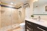 Bathroom featuring a walk-in shower with stone tile surround, pebble-style floor, and glass enclosure, complemented by a dark-finish vanity with a lig