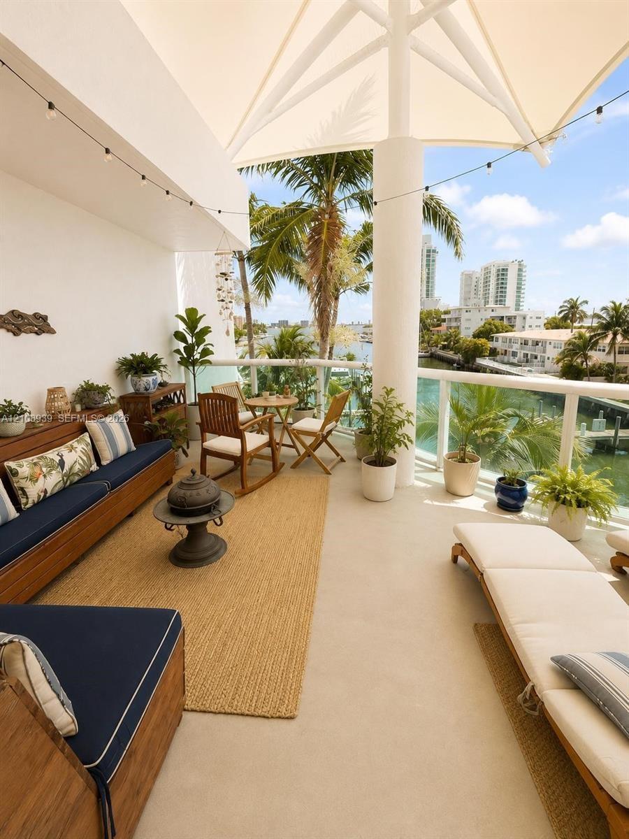 Covered terrace featuring a tensile fabric shade structure, glass panel railing, and concrete flooring, overlooking a water-facing landscape with matu