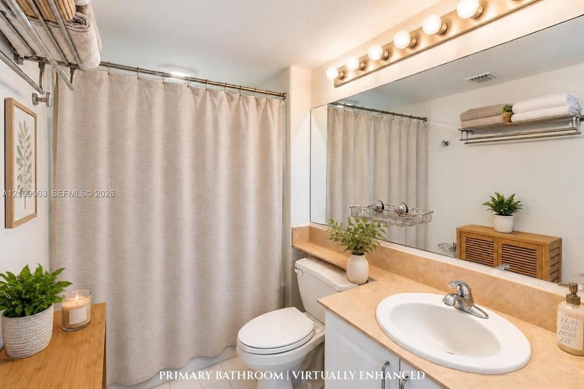 Bathroom featuring a vanity with a neutral-tone countertop, oval undermount sink, expansive wall-to-wall mirror, multi-bulb vanity lighting, and a sho
