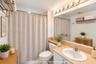 Bathroom featuring a vanity with a neutral-tone countertop, oval undermount sink, expansive wall-to-wall mirror, multi-bulb vanity lighting, and a sho