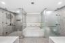 A luxurious spa-like sanctuary showcasing sleek contemporary cabinetry, expansive mirrors, a freestanding soaking tub, and beautifully coordinated des