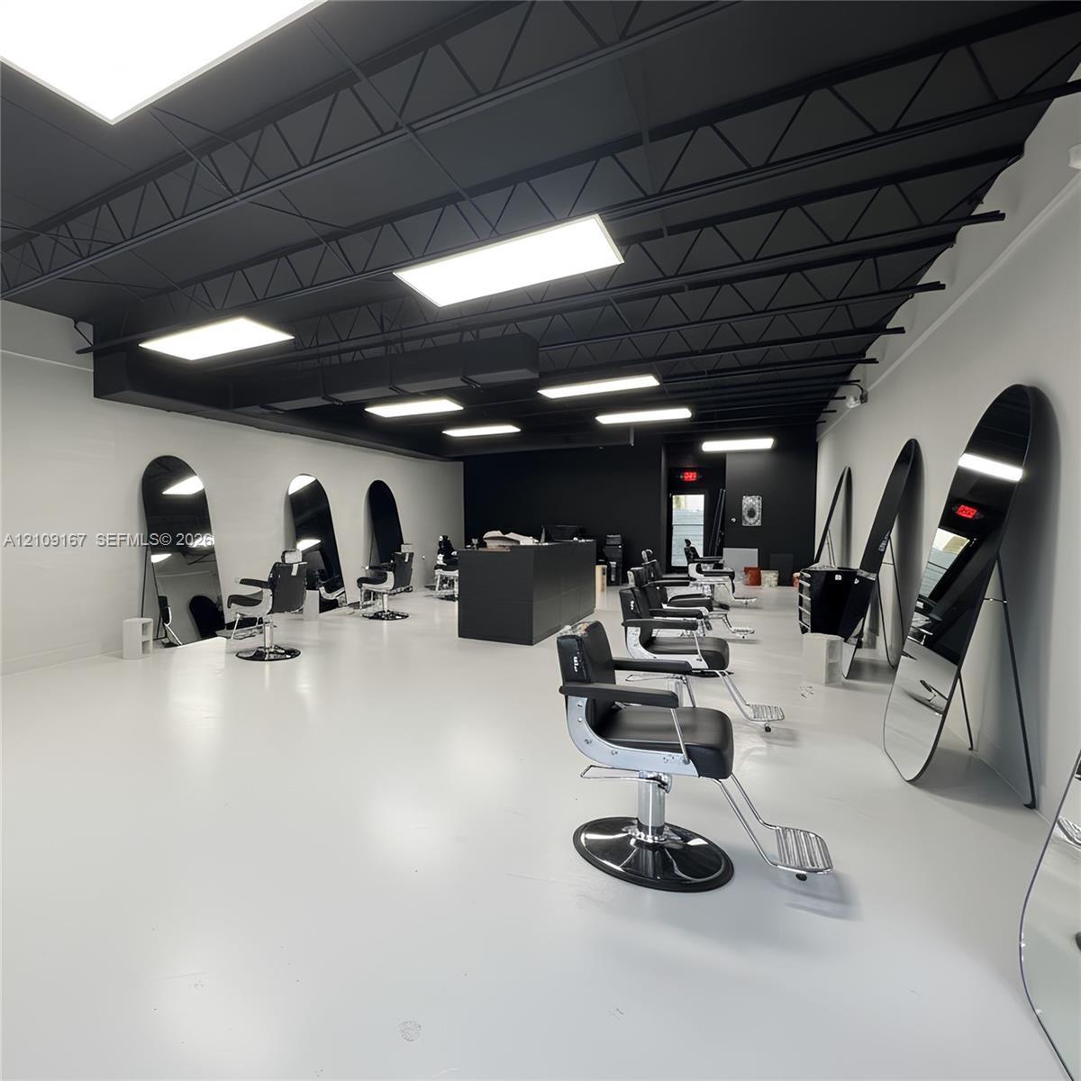 Open-concept interior featuring high-contrast black exposed ceiling trusses, bright rectangular LED panel lighting, polished light-reflective flooring