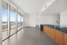 Floor-to-ceiling windows with access to an exterior terrace, large format tile flooring, and a kitchen island featuring wood-finish cabinetry, a dark 