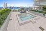 Rooftop terrace featuring an integrated tiled spa, built-in planters with evergreen shrubbery, and expansive glass railings overlooking the water