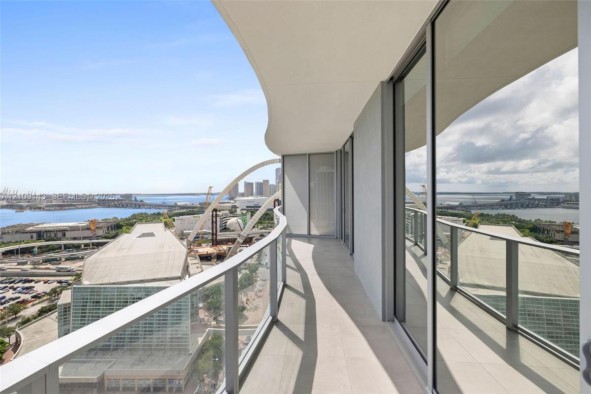 Curved private balcony featuring large-format stone flooring, glass panel railings, and floor-to-ceiling sliding glass doors