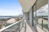 Curved private balcony featuring large-format stone flooring, glass panel railings, and floor-to-ceiling sliding glass doors