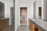 Floating vanity with natural wood-finish cabinetry, stone countertop, integrated rectangular sink, full-height LED-backlit mirror, and custom walk-in 