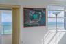Floor-to-ceiling sliding glass doors, multi-pane window with horizontal blinds, and private balcony with metal railing, showcasing an expansive ocean 