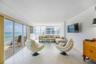 Living area featuring neutral tile flooring, expansive floor-to-ceiling glass sliding doors, wrap-around window configurations, and a private balcony 