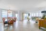 Open-concept main living area featuring light-toned tile flooring, oversized windows, multi-pane sliding glass doors, and a decorative crystal chandel