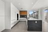 Kitchen featuring flat-panel white cabinetry, wood-finish upper cabinets, expansive waterfall-edge stone island, built-in wall oven, and large-format 