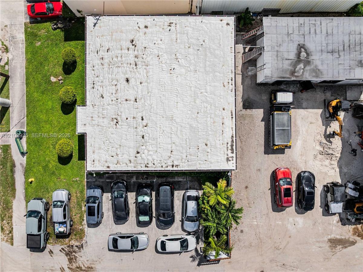 Aerial perspective featuring a commercial structure with an expansive paved surface area, dedicated on-site parking spaces, and manicured green space