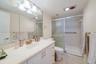 White vanity cabinetry featuring a light-toned countertop with integrated sink, full-width mirror, five-bulb integrated vanity lighting, and walk-in s