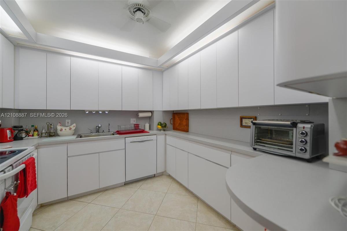 Kitchen featuring floor-to-ceiling white cabinetry, solid-surface countertops, integrated under-cabinet lighting, stainless steel sink with metal fauc