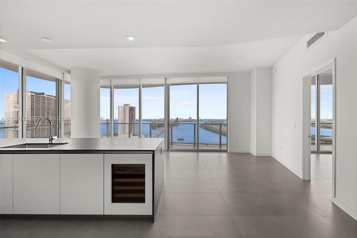 Kitchen island with stone-finish countertop, undermount sink, integrated wine cooler, and expansive floor-to-ceiling windows featuring water scenery