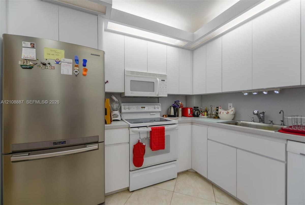 Kitchen featuring floor-to-ceiling white cabinetry, integrated recessed lighting, stainless steel refrigerator, white electric range with over-the-ran
