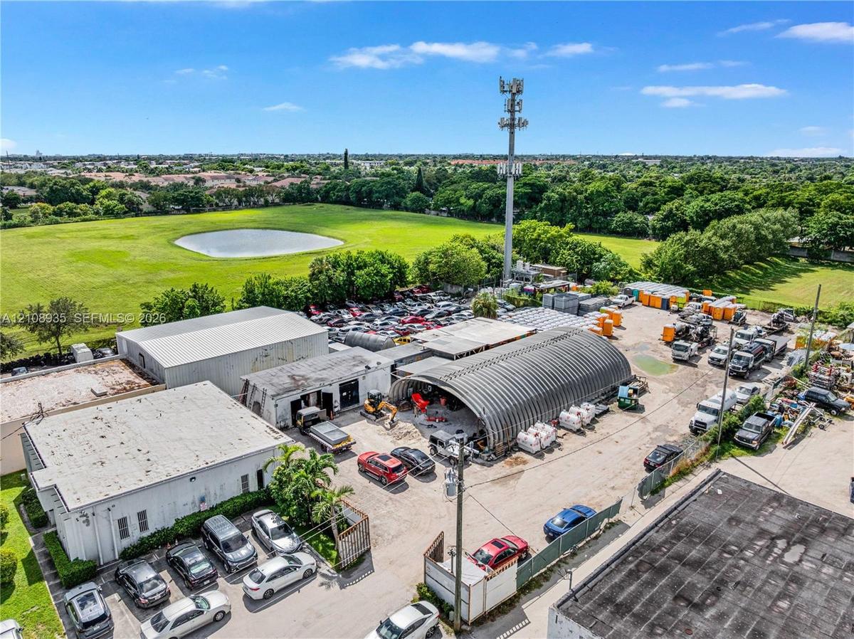 Industrial property featuring multiple structures including a semi-cylindrical metal warehouse, expansive exterior paved lot, and perimeter fencing