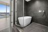 Freestanding soaking tub set within a glass-enclosed wet room featuring floor-to-ceiling dark-toned stone-finish tile and polished chrome plumbing fix