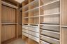 Custom walk-in closet featuring extensive wood-finish shelving, multiple integrated drawers, tiered angled shoe storage, and matte black hanging rods