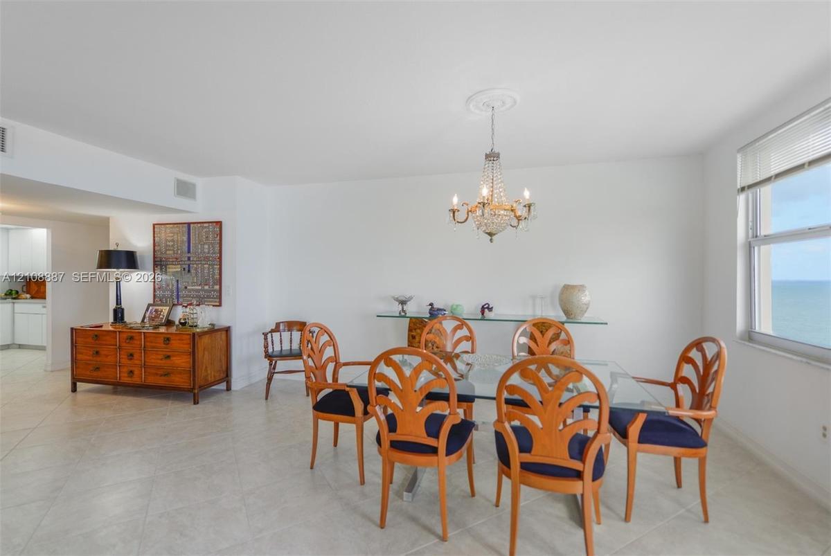 Open-concept living space featuring large-format tile flooring, a decorative crystal chandelier with ceiling medallion, and oversized windows providin