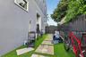 Side exterior featuring grey stucco siding, synthetic turf ground cover, concrete paver pathway, and vertical metal privacy fencing