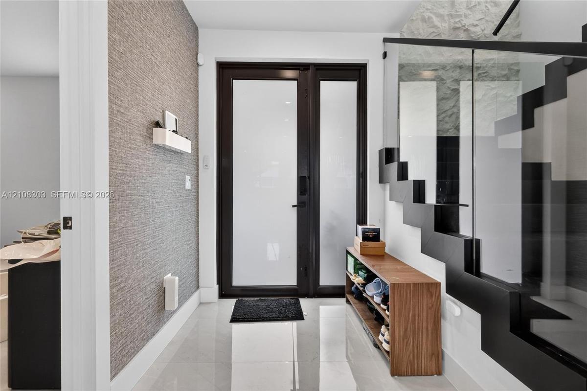 Entryway featuring a black-framed glass entry door, large-format tile flooring, textured wall covering, and a staircase with open risers and a glass r
