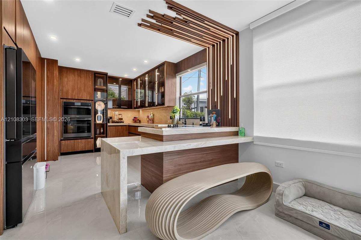 Custom wood cabinetry, stone-surfaced waterfall island, built-in double oven, and decorative wood-slat wall feature with integrated lighting