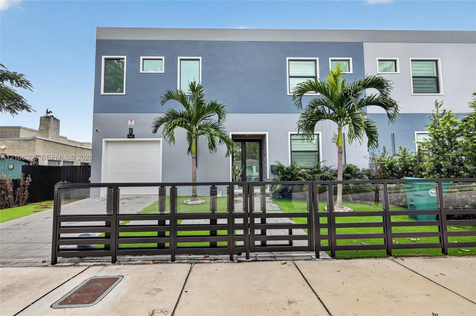 Modern two-story exterior featuring multi-tonal stucco facade, horizontal slat metal fencing, integrated single-car garage, and paved walkway