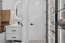 Bathroom featuring a white vanity with matte black hardware, integrated backlit oval mirror, wood-tone wall-mounted cabinet, and built-in shelving wit