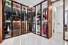 Custom built-in wardrobe featuring full-height glass-paneled doors, integrated LED accent lighting, wood-finish cabinetry, matte black hardware, and p