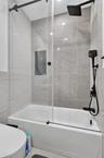 Shower and bathtub combination featuring large-format stone-finish tile surround, glass panel enclosure, matte black rainfall showerhead, and matching
