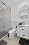 Walk-in shower with a sliding glass door, white wall-mounted vanity with two drawers, matte black hardware, oval-framed mirror, and large-format tile 