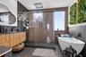 Bathroom featuring a floating wood-finish vanity with a dark countertop, a walk-in glass-enclosed shower with a rainfall showerhead, a freestanding so