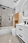 Bathroom featuring a white two-drawer vanity with matte black hardware, a shower-tub combination with a glass sliding door, large-format tile surround